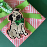 Pug ornament with a green bow tie on a pink and white patterned gift with a green ribbon.