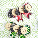 Red and green bow-shaped decorative trays filled with assorted holiday cookies on a patterned background.
