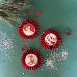 Set of three retro-style ruffled paper Christmas ornaments featuring vintage illustrations of a reindeer, Santa in his sleigh, and a snowman, accented with red pleated borders and hanging ribbons