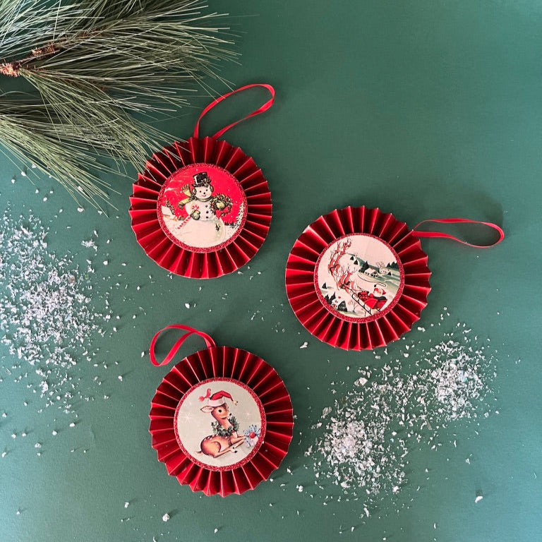 Set of three retro-style ruffled paper Christmas ornaments featuring vintage illustrations of a reindeer, Santa in his sleigh, and a snowman, accented with red pleated borders and hanging ribbons