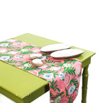 Pink and green seashell-patterned table runner displayed on a green table with decorative shells and plates.