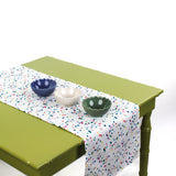 White confetti-pattern table runner on a green table styled with three decorative bowls.