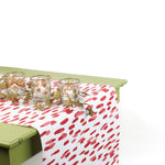 a green table covered by a white and red paper table runner featuring a brushtroke pattern called Club House by Madcap Cottage