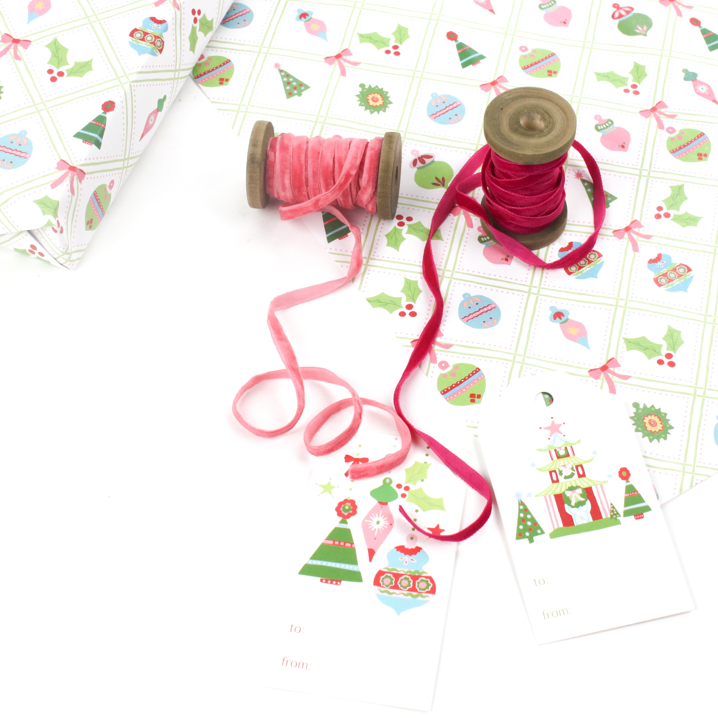 Holiday wrapping paper with Christmas ornament pattern displayed with ribbon spools and gift tags.