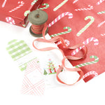 Styled display of red candy cane wrapping paper with ribbons and assorted gift tags.