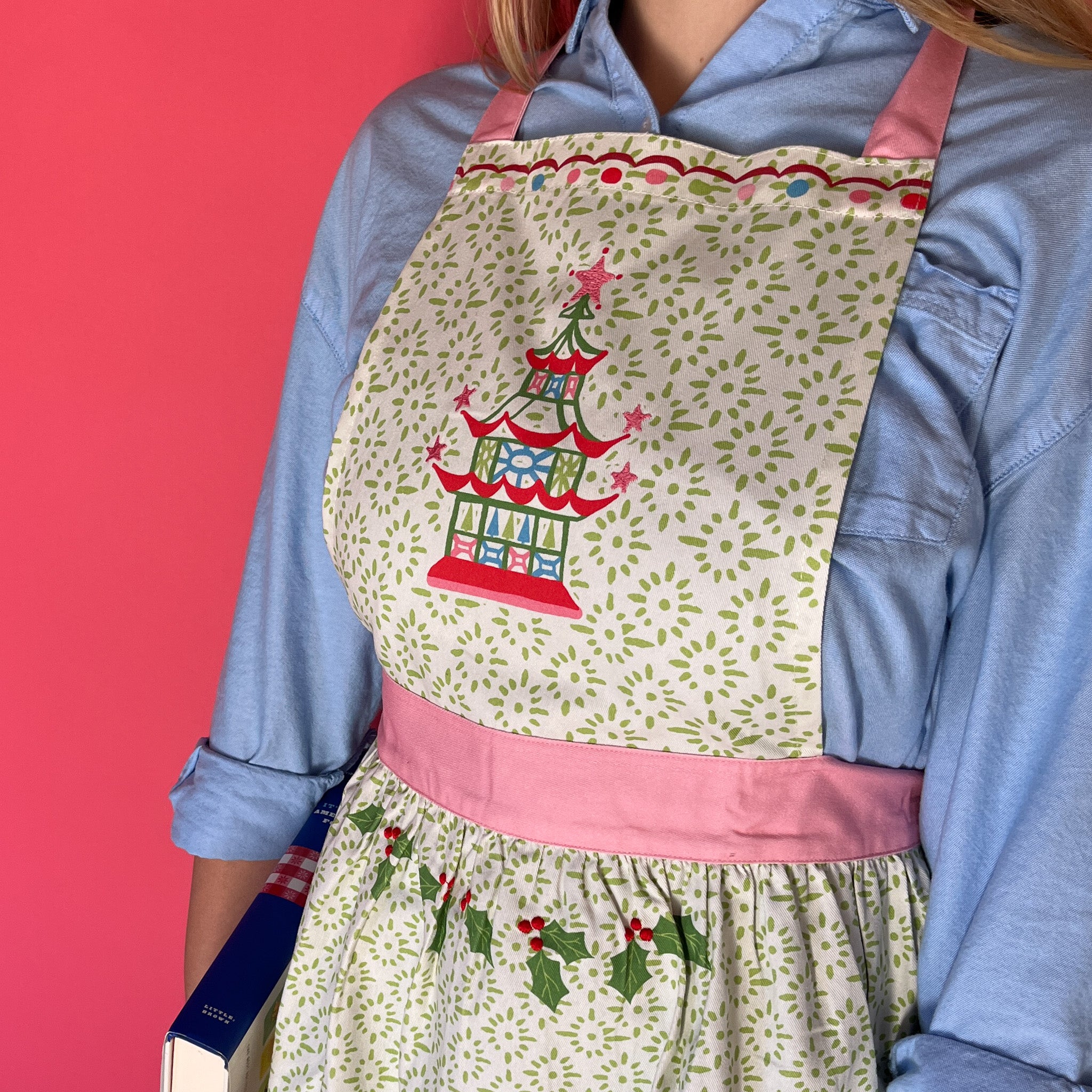 Person wearing Madcap cottage apron with pagoda design and pink straps on a red background