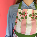 Person wearing a festive apron with holly design against a pink background
