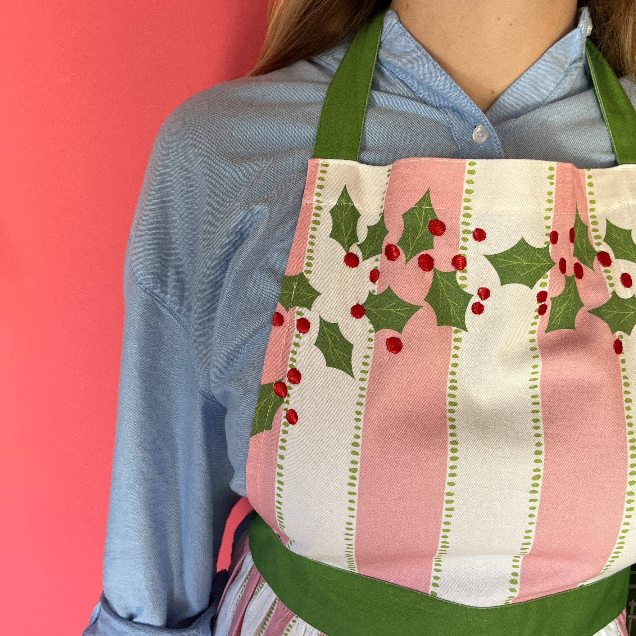 Person wearing a festive apron with holly design against a pink background