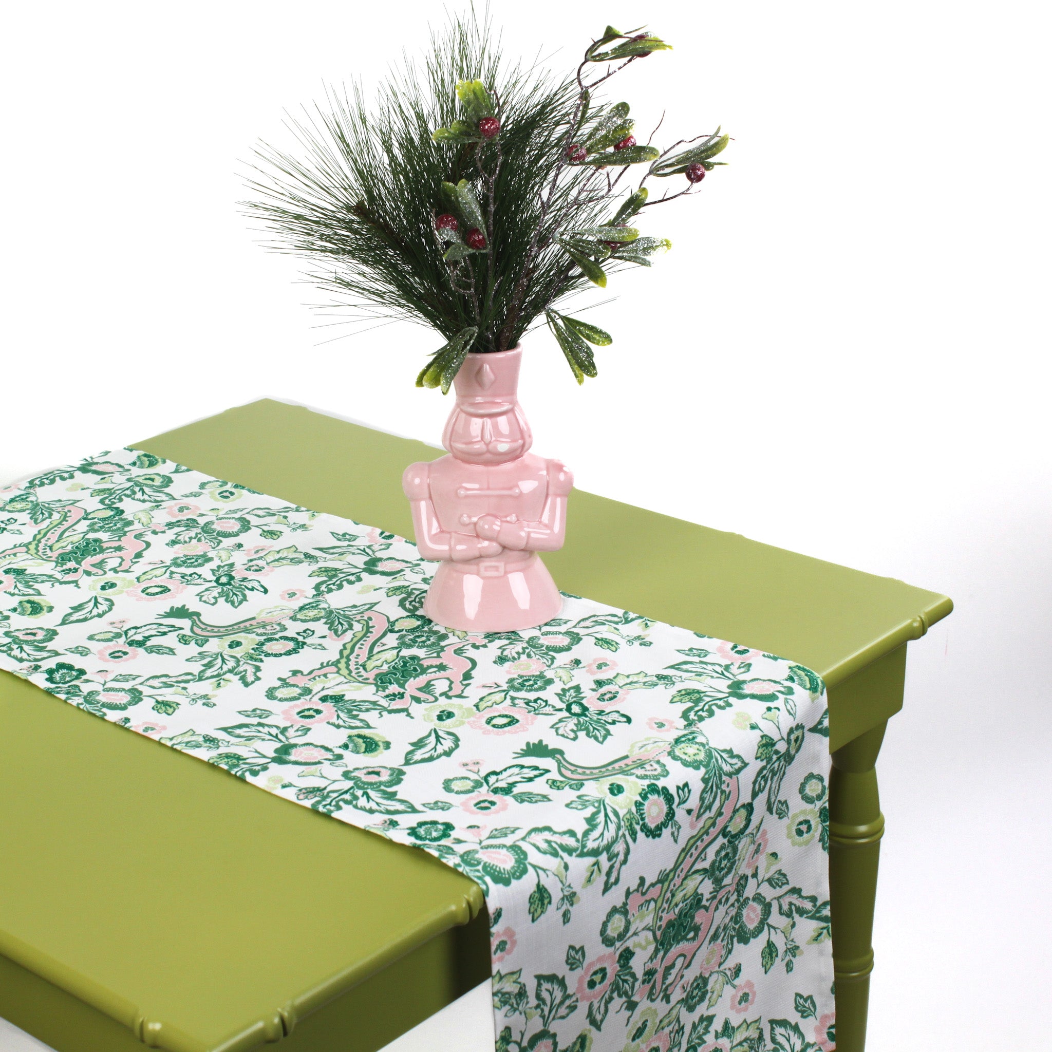 Floral table runner styled on a green table with a pink decorative vase and greenery.