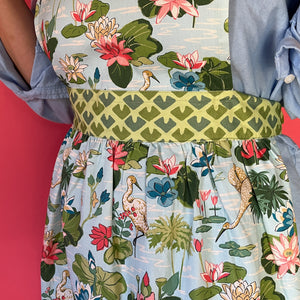 A person wearing the madcap cottage apron with floral and bird pattern on a red background