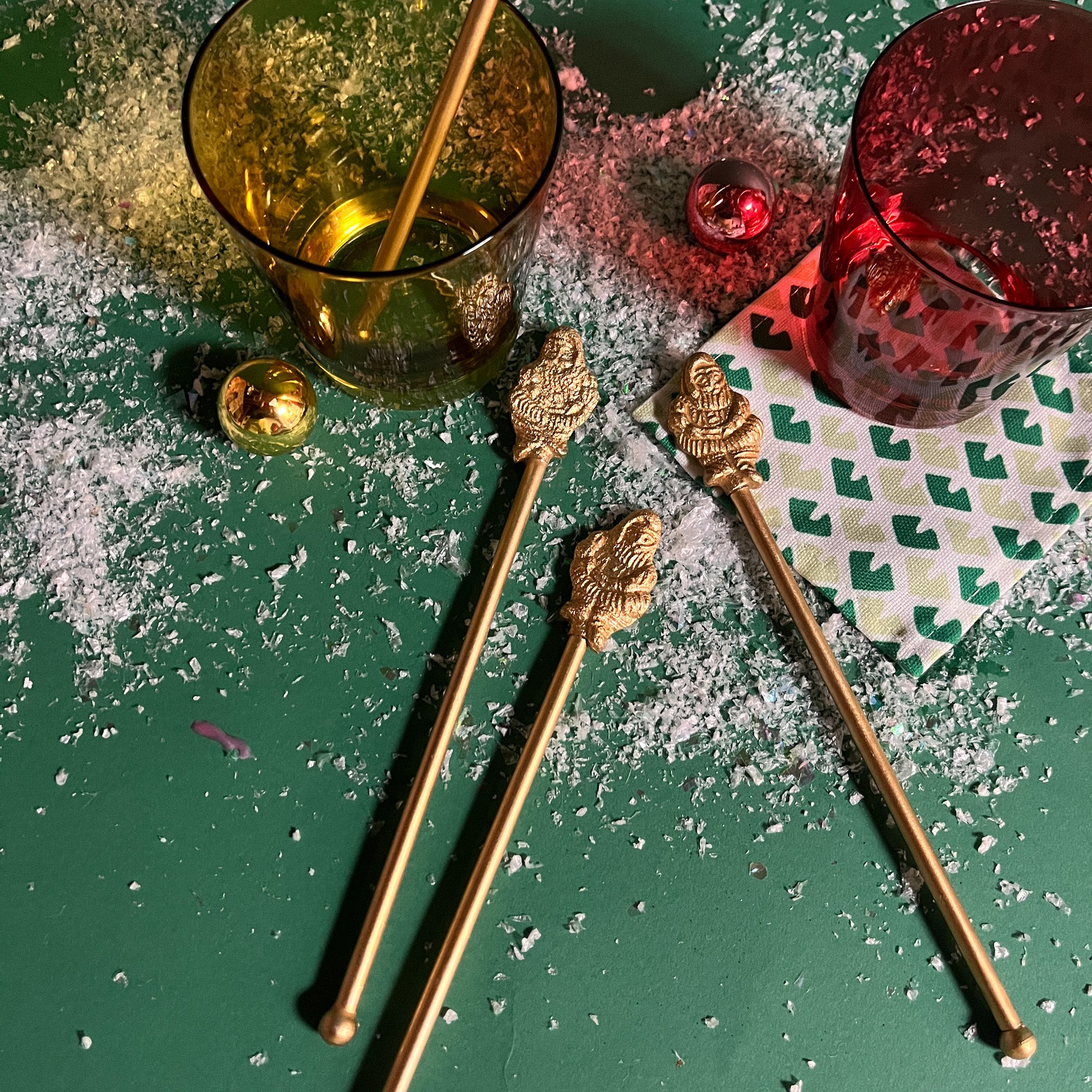 4 gilt metal gold christmas swizzle sticks with decorative santa ends on a green surface