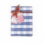 A pink gingham patterned gift tag with a white space attached to a wrapped present