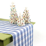 a green table covered by a Gin Lane Blue Gingham Paper Table Runner on a white background with white crhistmas tree centerpiece