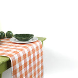 a green table covered with a gingham orange paper table runner in a pattern called gin lane by madcap cottage