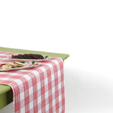 a green table covered with a Gin Lane Pink Gingham Paper Table Runner with a ceramic plate and cookies on top of it