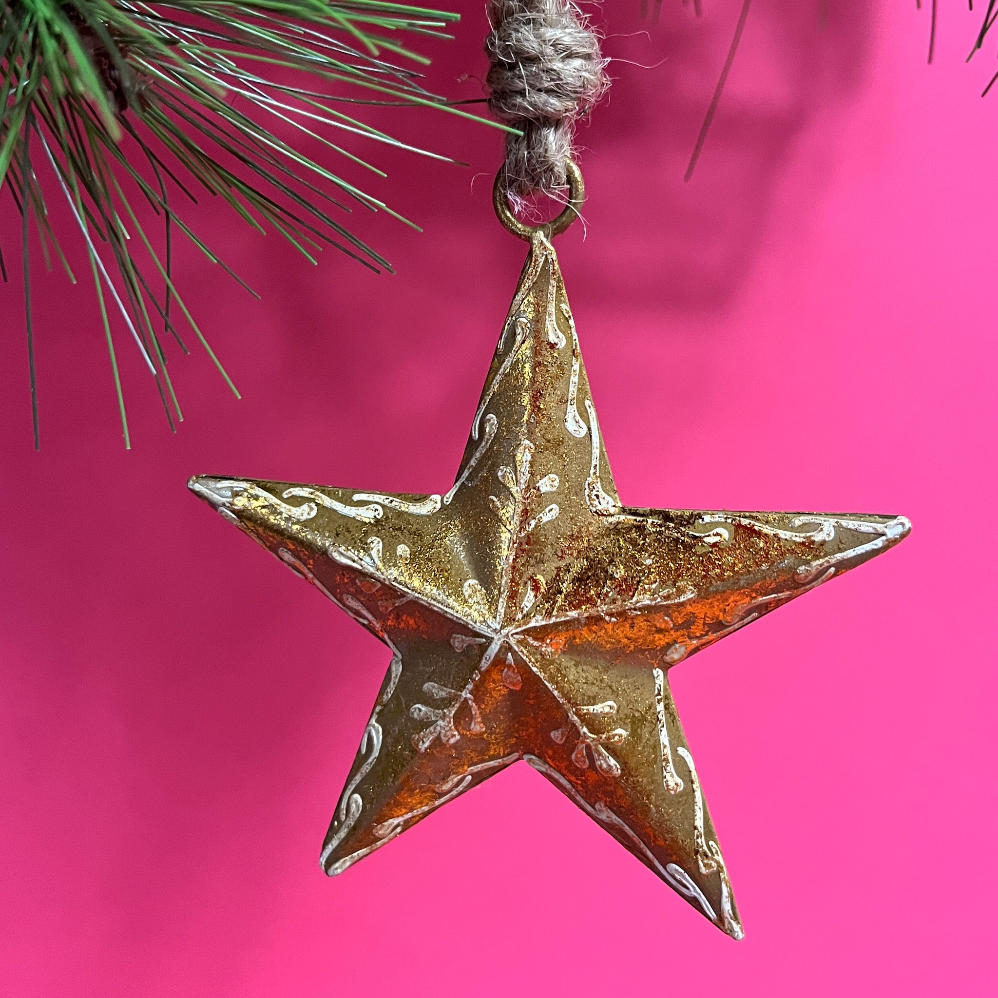 a gold star ornament hanging on a christmas tree branch against a red background. 