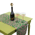 Green and pink patterned table runner displayed on a table with a bottle of sparkling drink and two glasses.