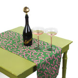 Green and pink patterned table runner displayed on a table with a bottle of sparkling drink and two glasses.
