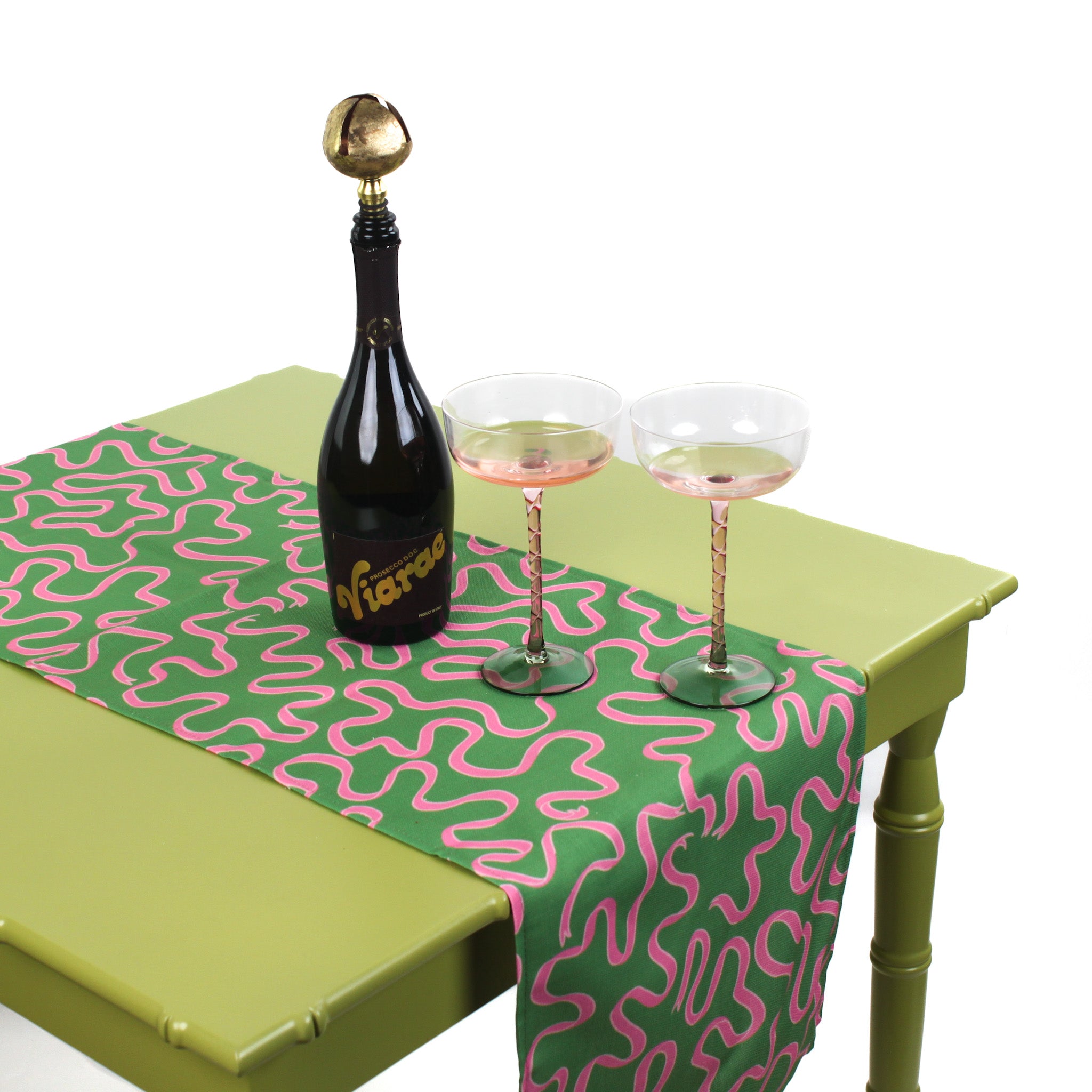 Green and pink patterned table runner displayed on a table with a bottle of sparkling drink and two glasses.