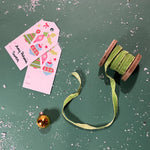 a light green Velvet Ribbon on Wood Spool in a green background with some gift tags on the side and gold ball ornaments