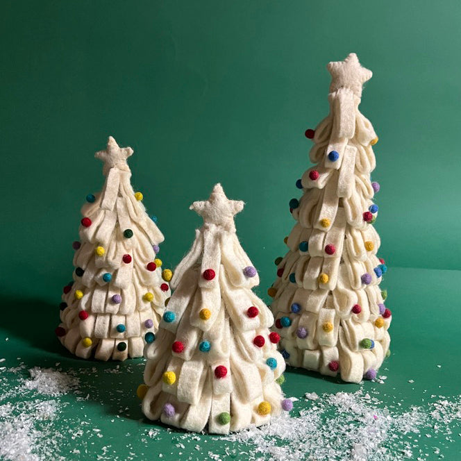 a set of three, white Looped Felt Christmas Tree Table Decorations with colourful bauble decorations, topped with stars against a green, snow scattered background. 