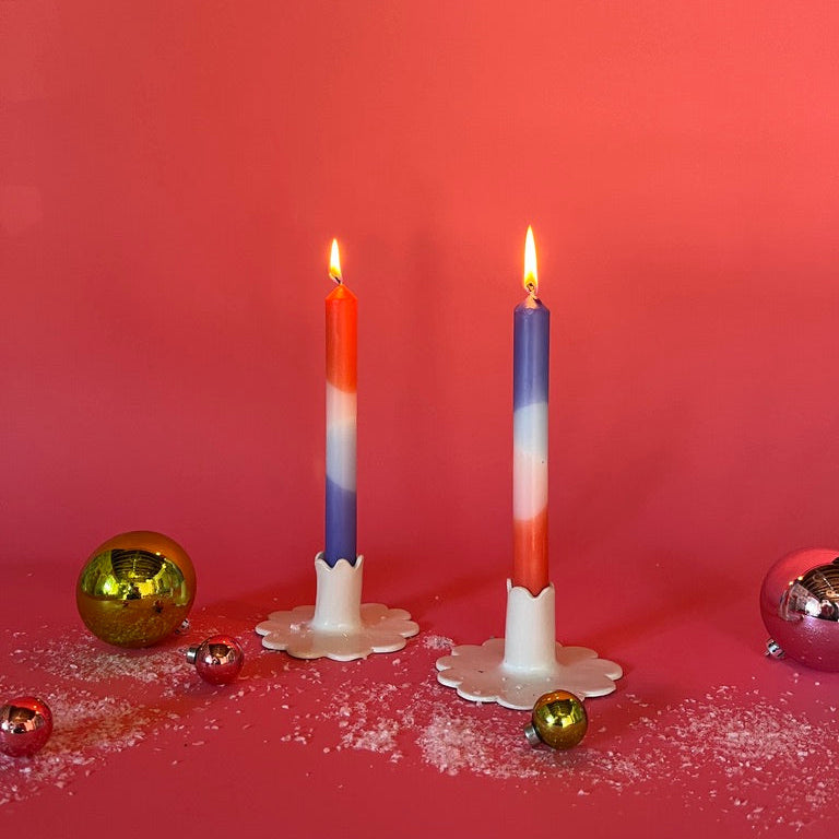 lighted 2 colorful taper candles in a mix of white, blue and orange in candle holders and with red background