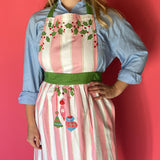 Person wearing a pink and white striped apron with Christmas designs against a red background