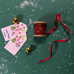 a red Velvet Ribbon on Wood Spool in a green background with some gift tags on the side and gold ball ornaments