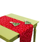 Red table runner with pink squiggle design displayed on a green table with two Christmas tree-shaped ceramic plates.
