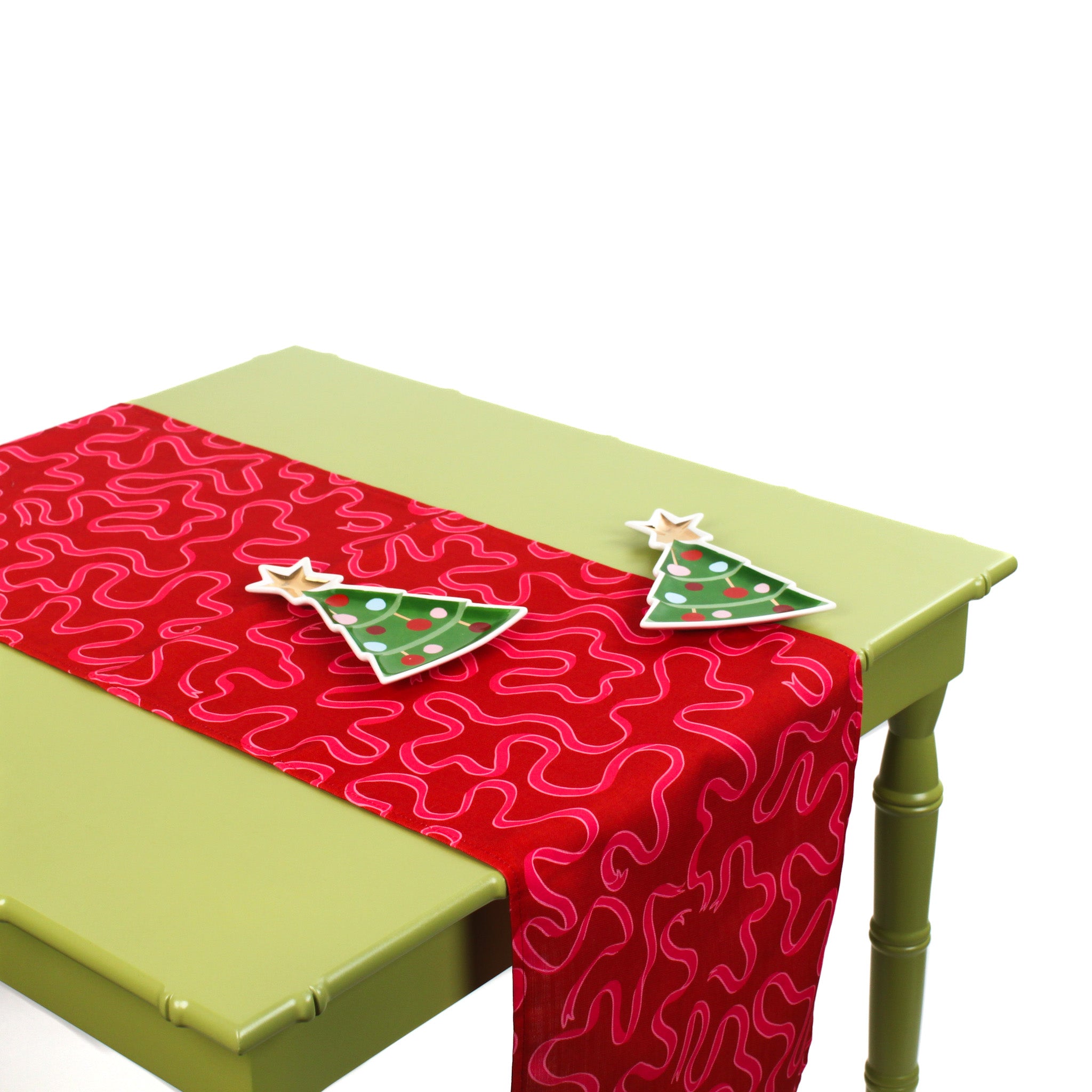 Red table runner with pink squiggle design displayed on a green table with two Christmas tree-shaped ceramic plates.