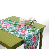 Snowflake-patterned table runner styled on a green table with mugs of marshmallows and a small spoon set.