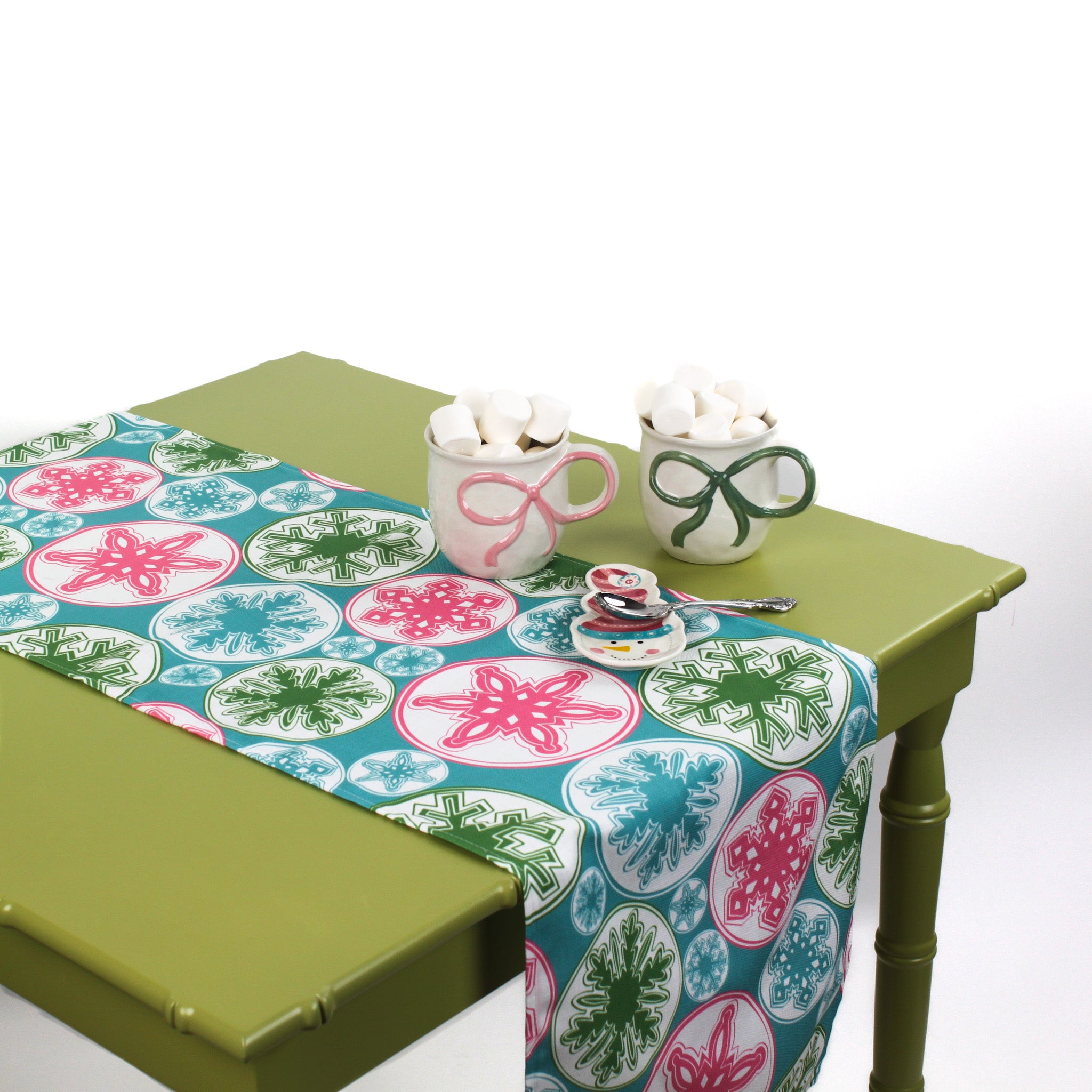 Snowflake-patterned table runner styled on a green table with mugs of marshmallows and a small spoon set.