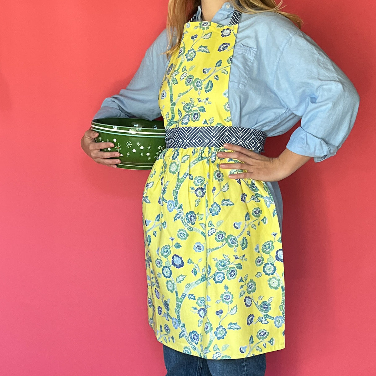 Person wearing a Madcap cottage yellow floral apron holding a green bowl against a red background