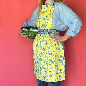 Person wearing a Madcap cottage yellow floral apron holding a green bowl against a red background