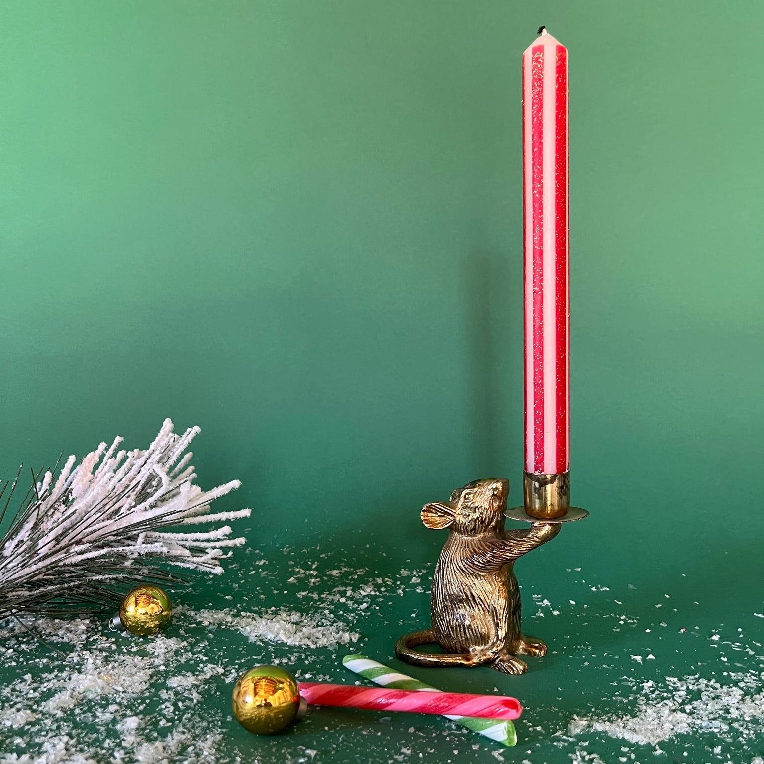 a gold red and white striped taper candle on a gold mice holder with a green background