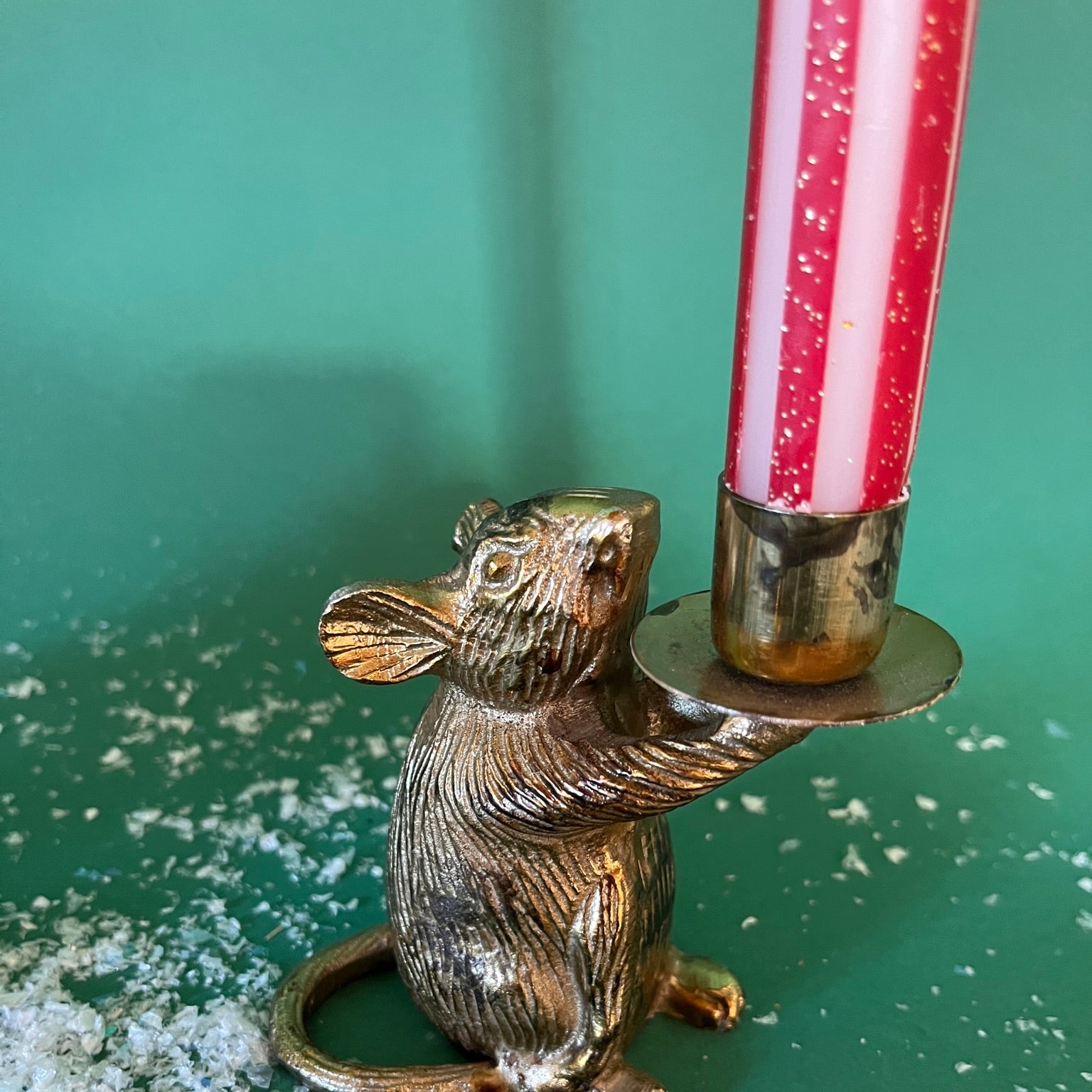 a gold red and white striped taper candle on a gold mice holder with a green background