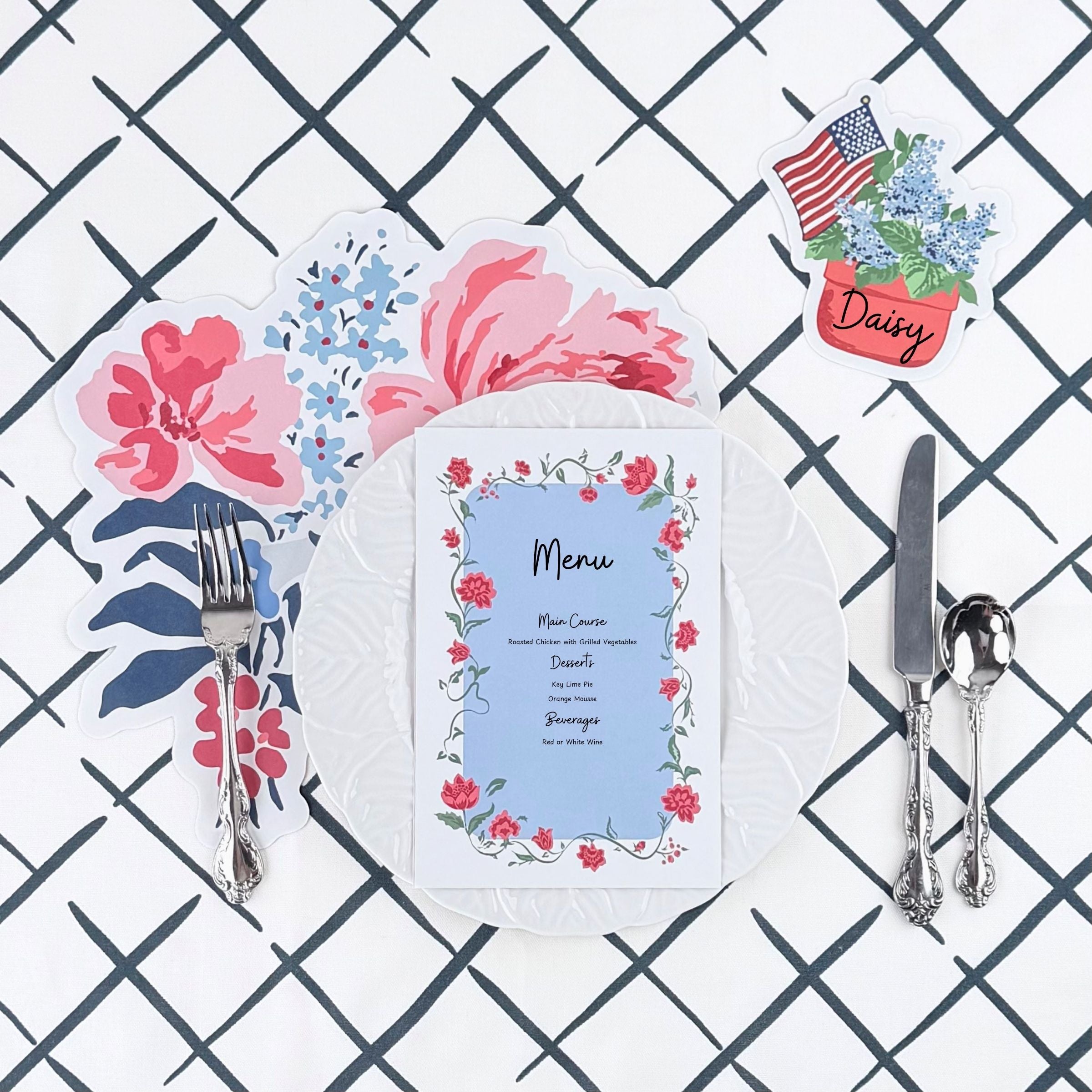 A styled floral table setting featuring a die cut floral paper placemat, white plate, floral menu card, decorative place card, and silver utensils on a navy trellis patterned background.
