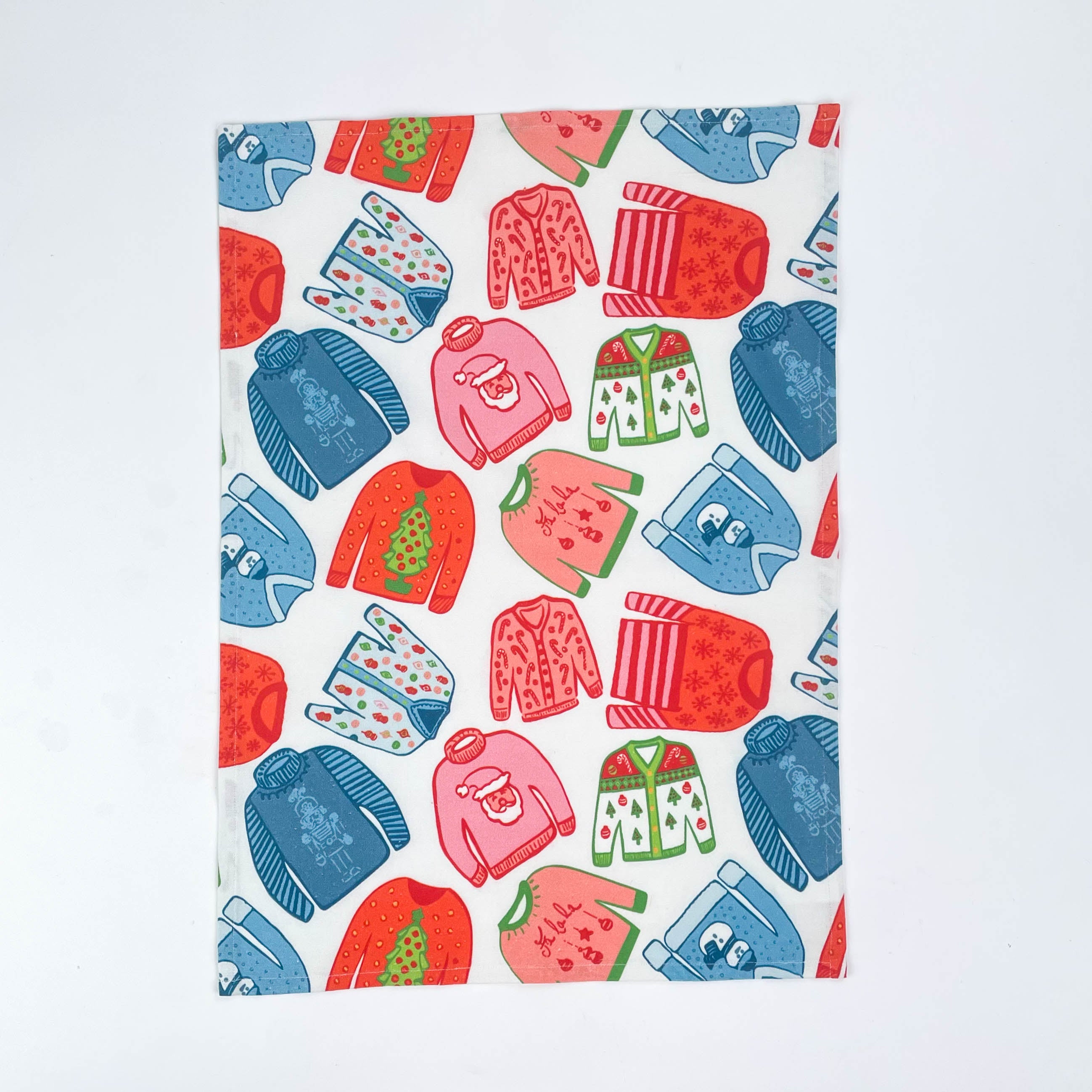 a madcap cottage christmas tea towel with colorful holiday sweater pattern in red, green and blue on a white background