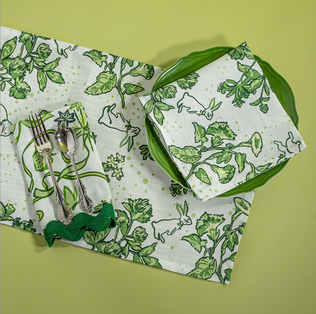 a springtime strawberry print fabric easter table runners in green with a plate, napkin and cutlery