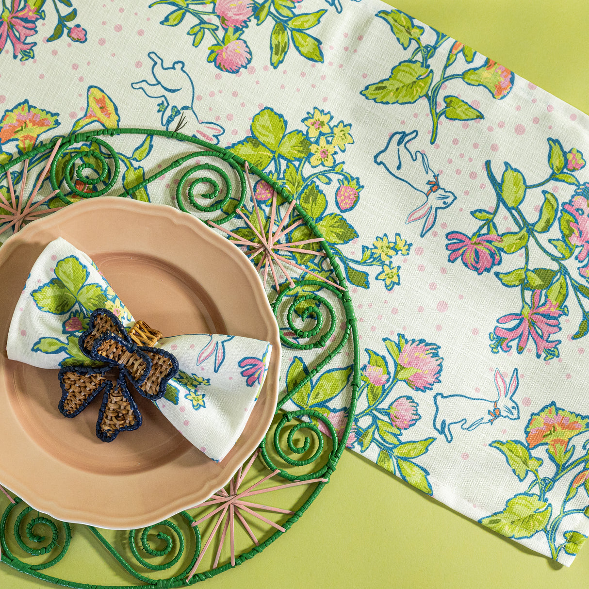 a bunny and strawberry print fabric easter table runners in multicolor with a round rattan charger on top. 