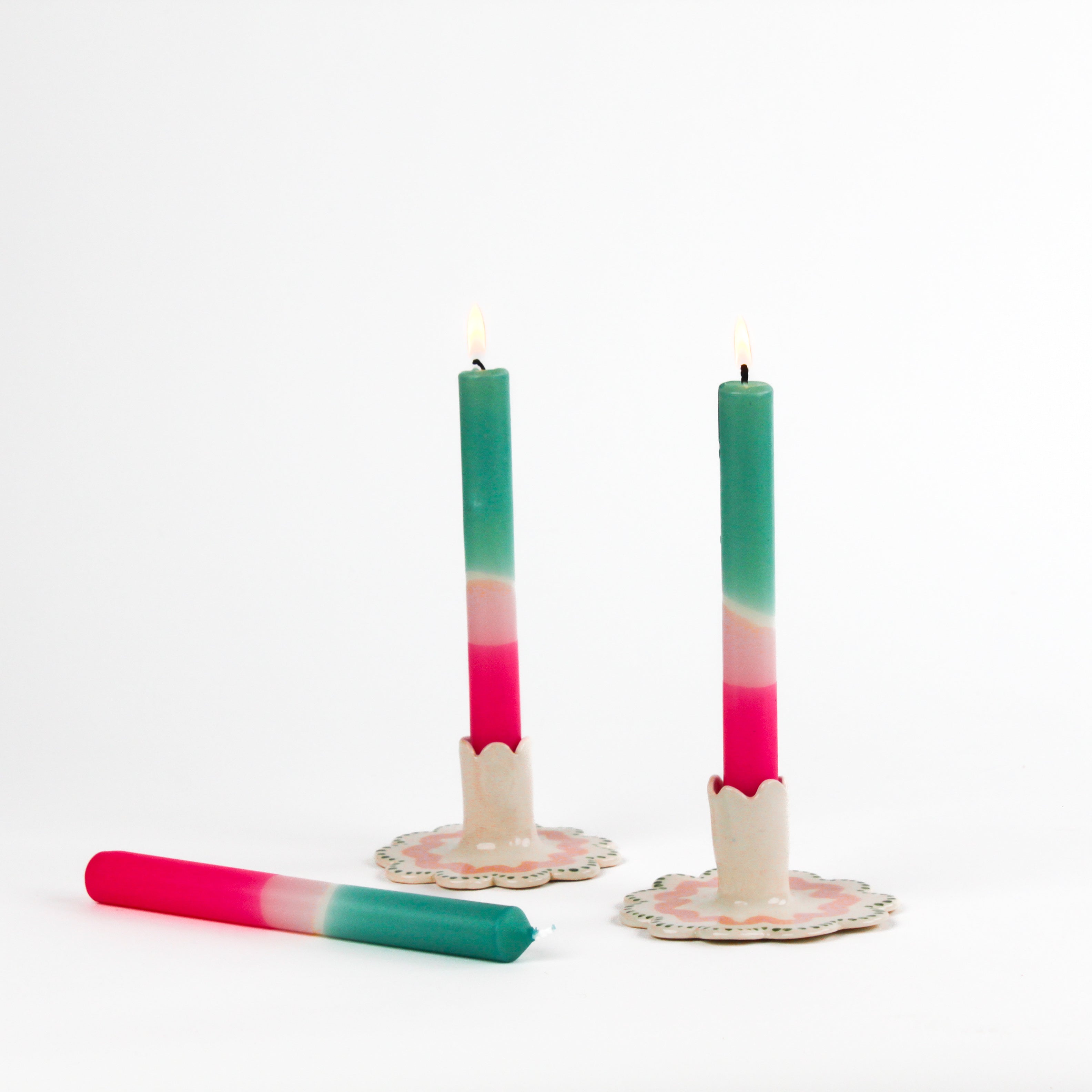 2 teal and pink taper candles in white ceramic candle holders and 1 candle lying down