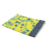 A yellow chinoiserie tea towel with a blue cherry blossom motif and a blue lattice pattern border against a white background. 