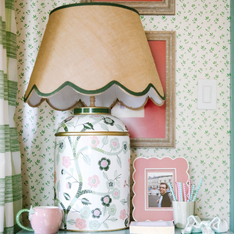 a pink and green chinoiserie lamp with a green trimmed scalloped rattan shade sitting on a blue nightstand. 