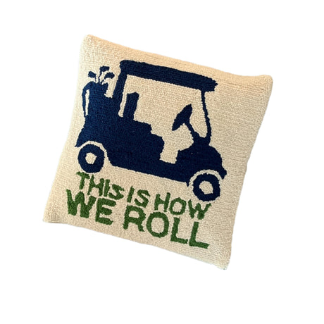 A white golf pillow with a blue golf cart and green text that reads THIS IS HOW WE ROLL