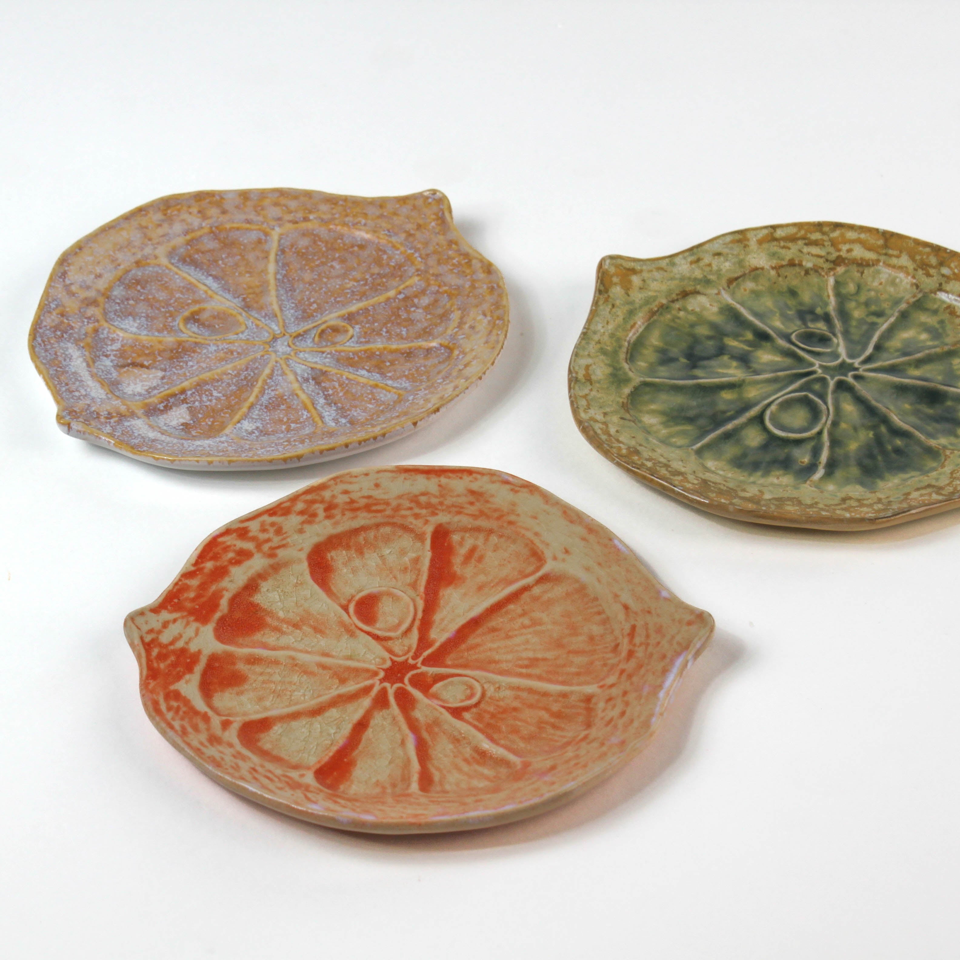 three citrus fruit shaped ceramic plates with decorative citrus patterns on a white background