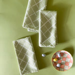 three light green dinner napkins in bahama court trellis print madcap cottage fabric next to a gingham plate with small candy eggs on it