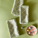 three light green dinner napkins in bahama court trellis print madcap cottage fabric next to a gingham plate with small candy eggs on it