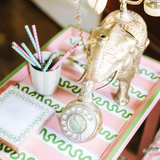 A pink side table with green and white striped accents and an elephant phone and notepad resting on top. 