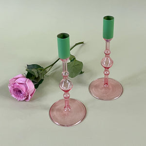 two pink glass candle holders with green tops with a pink rose behind them