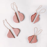 Set of folded flat pink paper Christmas ornaments in assorted bulb shapes with hanging strings, shown partially opened and ready for assembly.